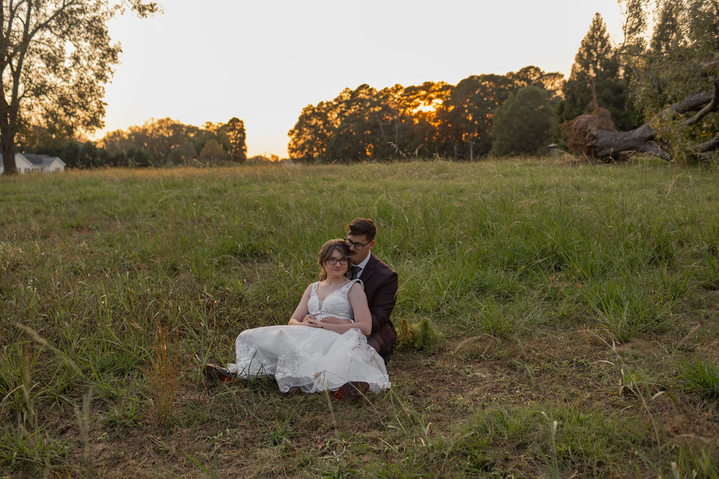 bride and groom sitting in field at the whiskey bonding farm in molena georgia